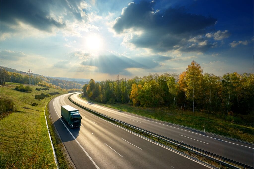 Vrachtwagen rijdt over een snelweg door een herfstlandschap terwijl de zon door de wolken breekt