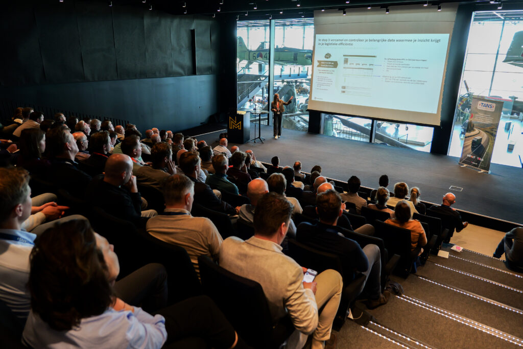 Volle zaal luistert naar een presentatie op groot scherm tijdens het TANS Kennisevent van 7 april 2026