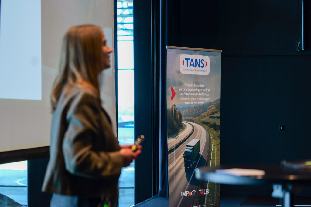 Spreker geeft een presentatie naast een TANS roll-up banner tijdens het Kennisevent van 7 april 2026