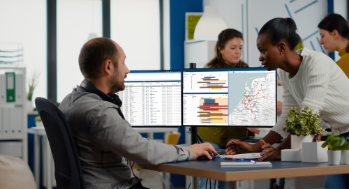 Planner en collega overleggen bij twee schermen met transportplanning en een kaart van Nederland