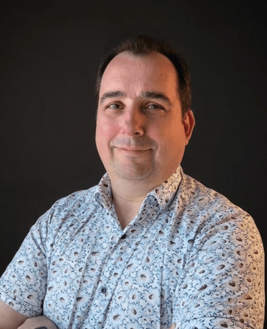 Portret van Arnold van TANS in een lichtblauw overhemd met gebloemd motief, armen over elkaar