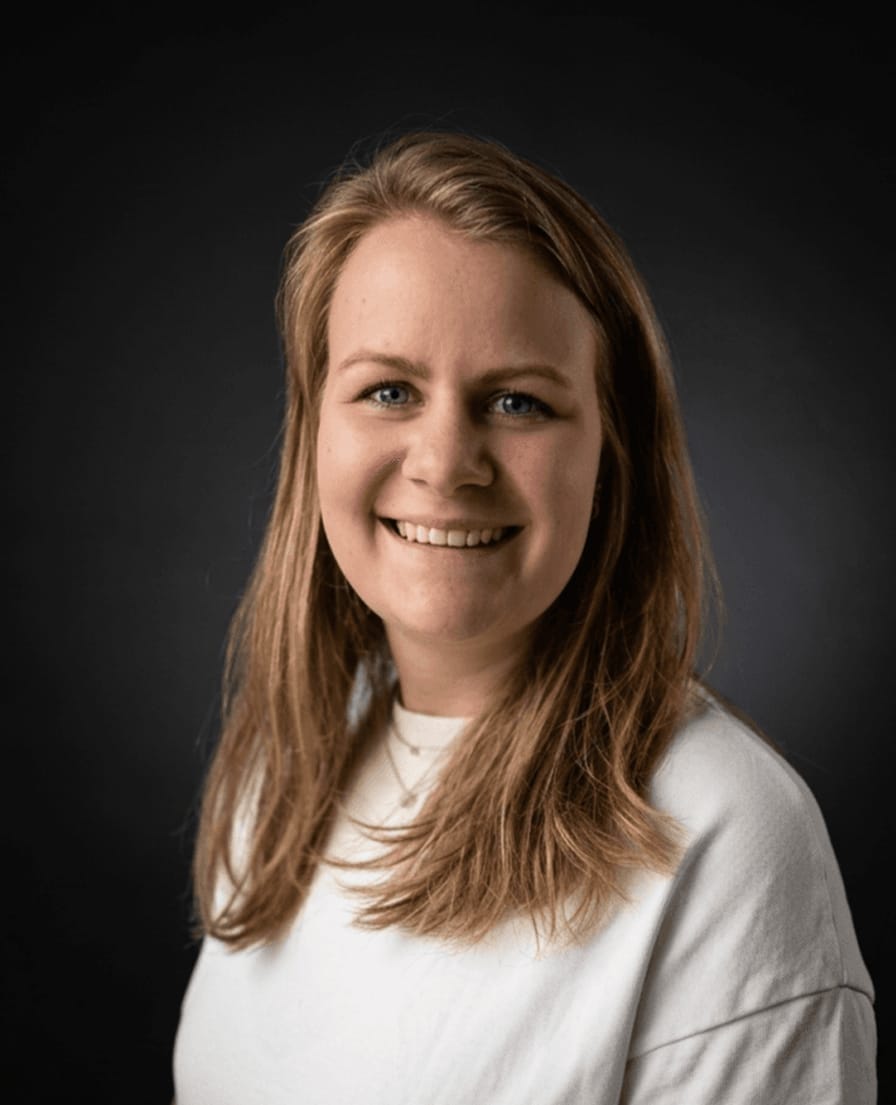 Portret van Ayla in een witte trui tegen een donkere achtergrond