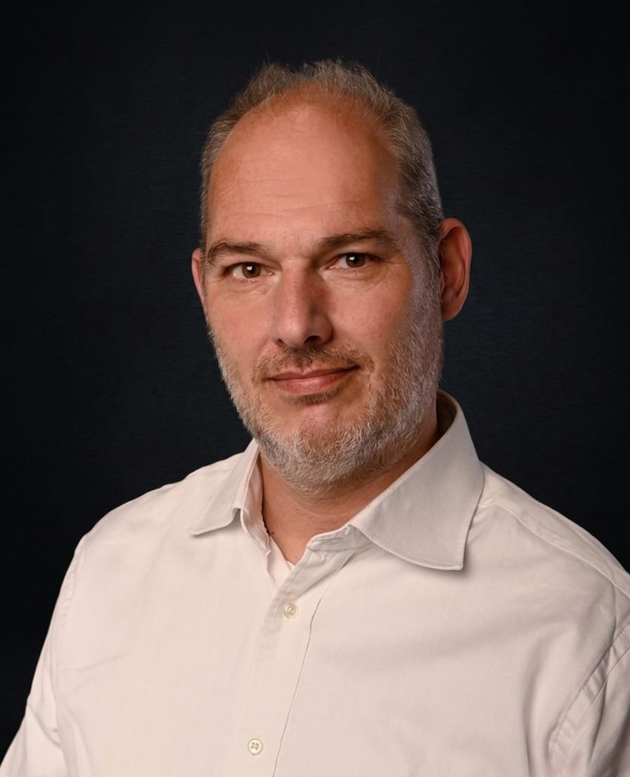 Portret van Pieter-Jan in een wit overhemd tegen een donkere achtergrond
