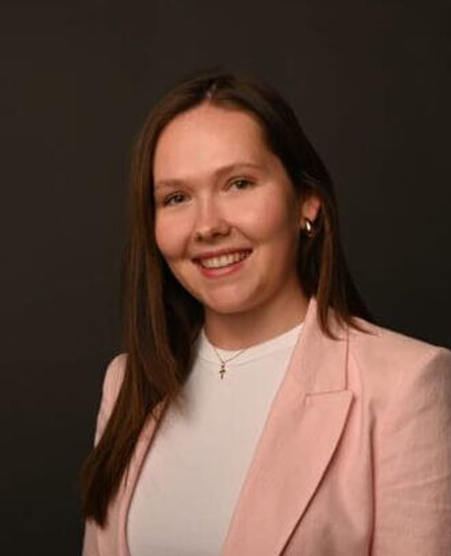Portret van Rosalie in een roze blazer en wit shirt tegen een donkere achtergrond